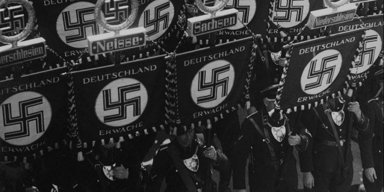 Los miembros de las SS llevan banderas con una esvástica y nombres de estados y ciudades alemanas mientras marchan hacia el ayuntamiento de Nuremberg, Alemania, el 10 de septiembre de 1935, para inaugurar la convención del Partido Nacional Socialista de los Trabajadores Alemanes. (Foto AP)