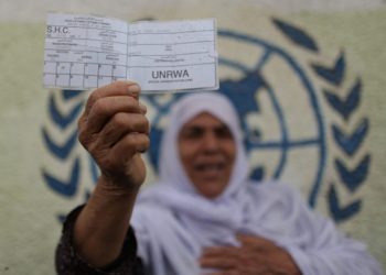 Una mujer palestina se para frente a la sede de UNRWA en la ciudad de Gaza con una tarjeta de racionamiento para refugiados durante una protesta que exige que la agencia de la ONU reanude la ayuda, el 8 de abril de 2013. Foto de Wissam Nassar / Flash90.