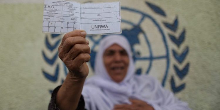 Una mujer palestina se para frente a la sede de UNRWA en la ciudad de Gaza con una tarjeta de racionamiento para refugiados durante una protesta que exige que la agencia de la ONU reanude la ayuda, el 8 de abril de 2013. Foto de Wissam Nassar / Flash90.