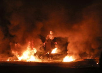 Un terrorista enmascarado tira un neumático en llamas durante un ataque nocturno cerca de la valla a lo largo de la frontera con Israel, al este de la ciudad de Gaza, el 11 de febrero de 2019. (Mahmud Hams / AFP)