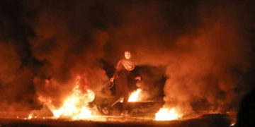 Un terrorista enmascarado tira un neumático en llamas durante un ataque nocturno cerca de la valla a lo largo de la frontera con Israel, al este de la ciudad de Gaza, el 11 de febrero de 2019. (Mahmud Hams / AFP)