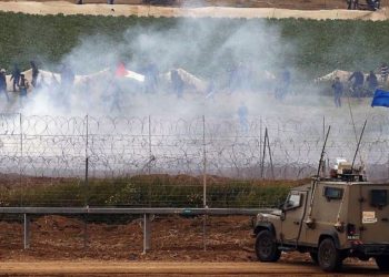 Vehículos militares israelíes mantienen su posición en la valla fronteriza mientras los palestinos ondean banderas nacionales se manifiestan para conmemorar el primer aniversario de las protestas de la "Marcha de retorno", el 30 de marzo de 2019. (Jack Guez / AFP)