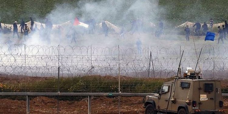 Vehículos militares israelíes mantienen su posición en la valla fronteriza mientras los palestinos ondean banderas nacionales se manifiestan para conmemorar el primer aniversario de las protestas de la "Marcha de retorno", el 30 de marzo de 2019. (Jack Guez / AFP)