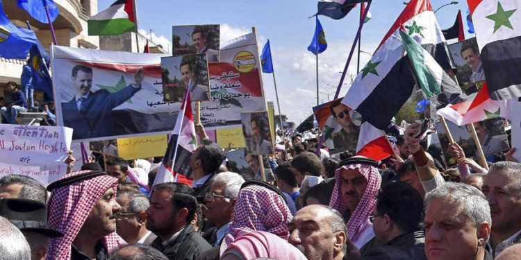 En esta foto publicada por la agencia de noticias oficial siria SANA, los sirios sostienen banderas nacionales y retratos del presidente sirio Bashar Assad durante una protesta contra el movimiento del presidente de Estados Unidos Donald Trump para reconocer la soberanía israelí sobre los Altos del Golán, en Homs, Siria, el 26 de marzo. 2019. (SANA via AP)