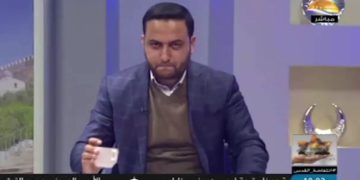 Un noticiero de la estación de televisión Al-Aqsa, afiliada a Hamas, coloca una taza sobre su escritorio en lo que el servicio de seguridad Shin Bet dice que era un código secreto para un operativo en Cisjordania. (Captura de pantalla: Al-Aqsa TV / Shin Bet)