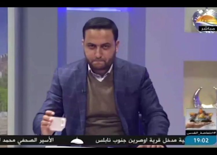 Un noticiero de la estación de televisión Al-Aqsa, afiliada a Hamas, coloca una taza sobre su escritorio en lo que el servicio de seguridad Shin Bet dice que era un código secreto para un operativo en Cisjordania. (Captura de pantalla: Al-Aqsa TV / Shin Bet)