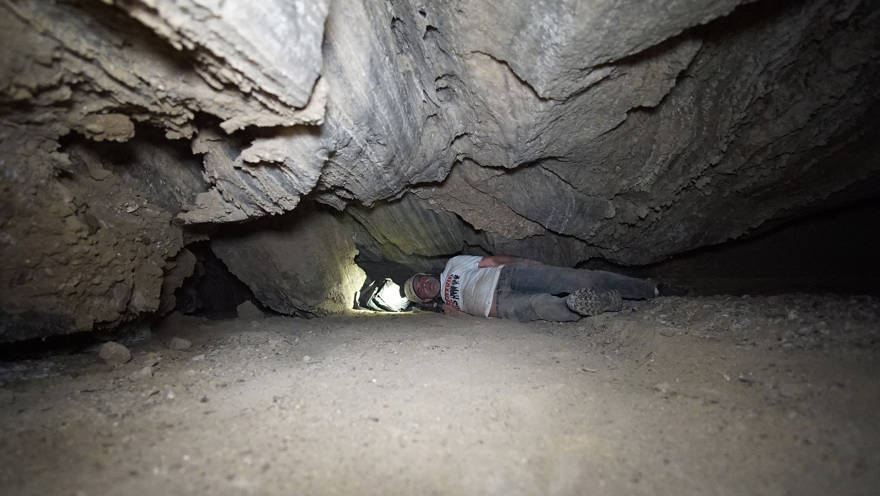 Un investigador pasa por una estrecha abertura en la cueva de Malcham el 22 de marzo de 2019, cerca del Mar Muerto. (Cortesía Anton Chikishev / Universidad Hebrea)
