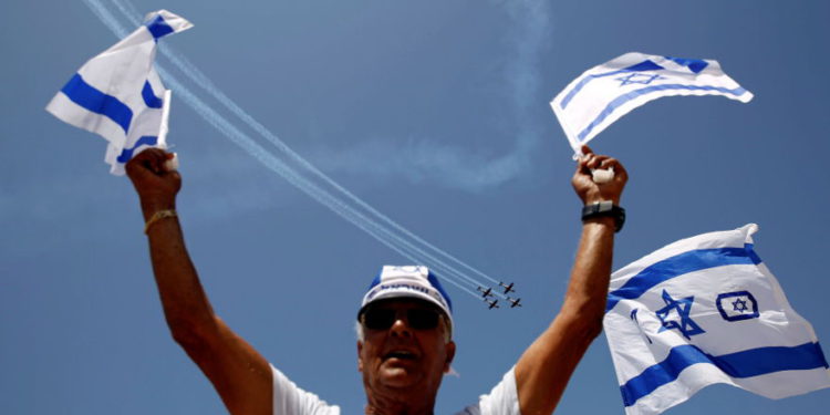 Un hombre ondea banderas de Israel mientras aviones de la Fuerza Aérea israelí vuelan en formación sobre el mar Mediterráneo durante un espectáculo aéreo como parte de las celebraciones por el Día de la Independencia de Israel con motivo del 70 aniversario de la creación del estado, en Tel Aviv, Israel, el 19 de abril. 2018 .. (crédito de foto: REUTERS / AMIR COHEN)