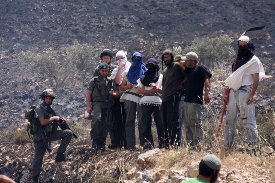 Colonos israelíes enmascarados de Yitzhar y soldados observan cómo los campos palestinos fueron incendiados en la aldea de Asira al-Qiblyia el 2 de junio de 2010. (Wagdi Ashtiyeh / Flash90)