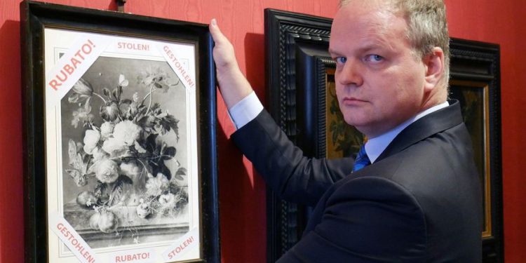 En esta foto, disponible el 1 de enero de 2019, Eike Schmidt, director de la Galería de los Uffizi, posa para una foto mientras sostiene una copia de un bodegón "Jarrón de flores", del artista holandés Jan van Huysum, con una escritura. en rojo, "robado", dentro de la galería de los Uffizi, en Florencia, Italia. (Oficina de prensa de la Galería Uffizi vía AP)