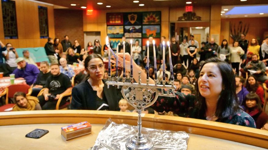 Alexandria Ocasio-Cortez (L) ayuda a encender una vela en una celebración de Hannukah el 9 de diciembre de 2018 (Judíos para la Justicia Racial y Económica / Twitter)
