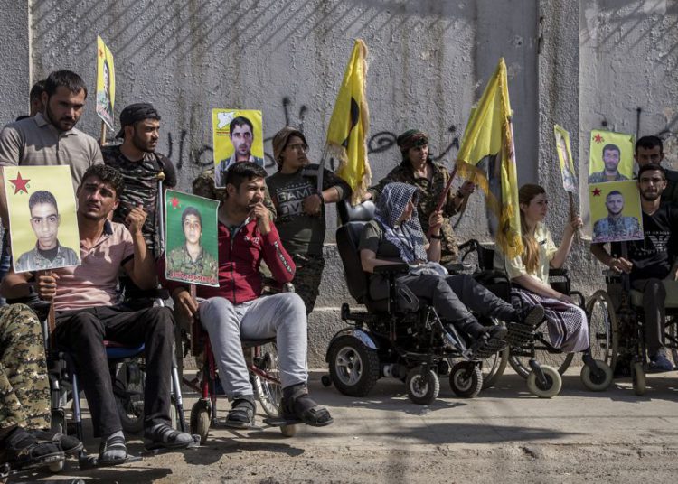 Los combatientes kurdos heridos tienen retratos de camaradas que fueron asesinados mientras luchaban contra el Estado Islámico, durante una manifestación contra una incursión turca prevista contra combatientes kurdos sirios, frente al edificio de las Naciones Unidas, en Qamishli, noreste de Siria, el lunes 8 de octubre de 2019. (Foto AP / Ahmad Baderkhan)