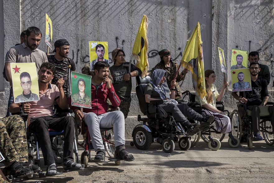 Los combatientes kurdos heridos tienen retratos de camaradas que fueron asesinados mientras luchaban contra el Estado Islámico, durante una manifestación contra una incursión turca prevista contra combatientes kurdos sirios, frente al edificio de las Naciones Unidas, en Qamishli, noreste de Siria, el lunes 8 de octubre de 2019. (Foto AP / Ahmad Baderkhan)