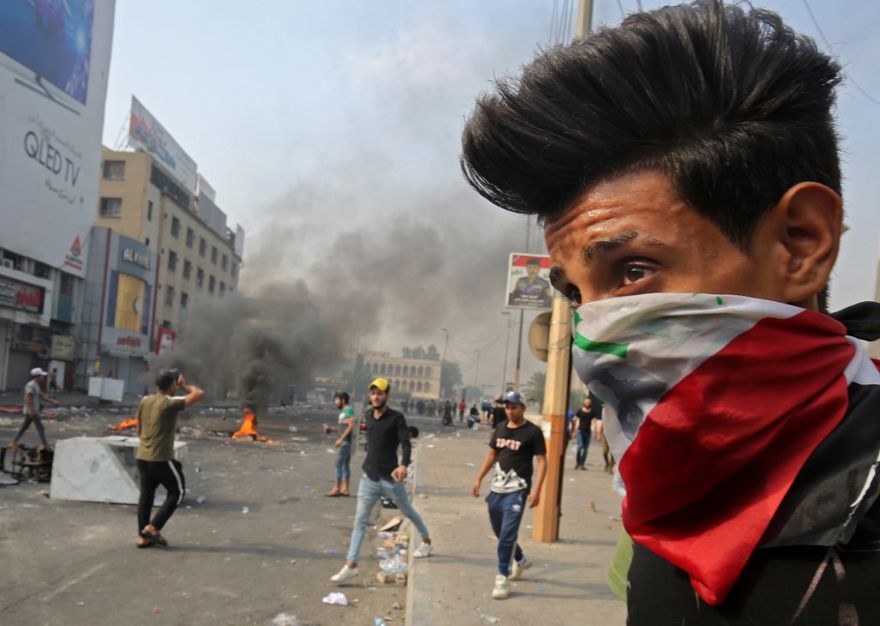 Un manifestante con una bandera nacional iraquí como una máscara facial de bandana se encuentra durante los enfrentamientos entre los manifestantes y la policía antidisturbios en medio de manifestaciones contra la corrupción estatal, el fracaso de los servicios públicos y el desempleo, en la céntrica plaza Tahrir de Bagdad, la capital iraquí, el 3 de octubre de 2019. (AHMAD AL -RUBAYE / AFP)