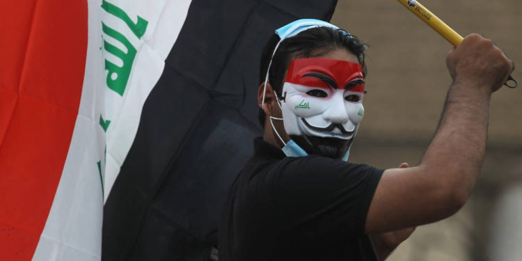 Un manifestante iraquí con una máscara de Guy Fawkes con los colores de la bandera nacional ondea una bandera iraquí durante una manifestación antigubernamental en la capital, Bagdad, el 27 de octubre de 2019. (AFP)