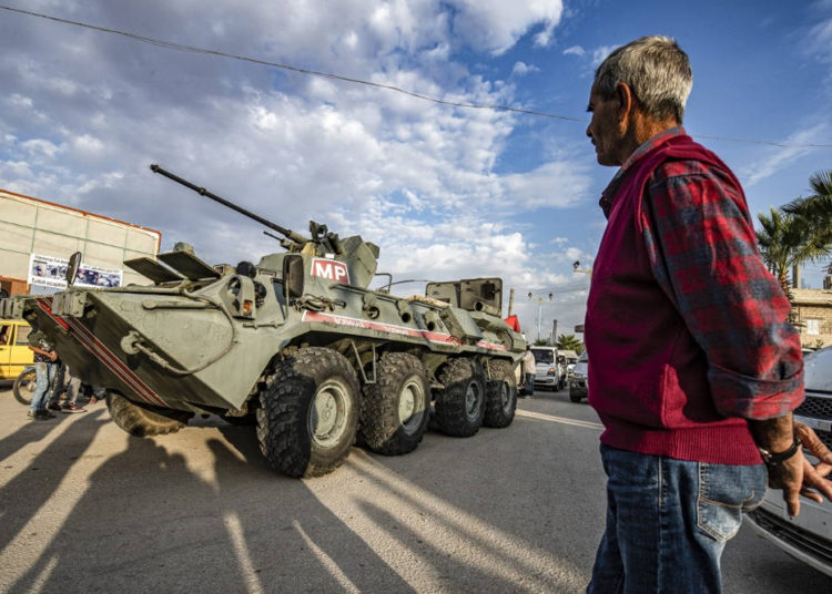 Un hombre mira cómo un vehículo blindado de la policía militar rusa pasa por una calle en la ciudad de Amuda, en el noreste de Siria, en la provincia de Hasakeh, el 24 de octubre de 2019, como parte de una patrulla conjunta entre las fuerzas rusas y las fuerzas de seguridad internas de los kurdos sirios cerca de la frontera con Pavo. (Delil SOULEIMAN / AFP)