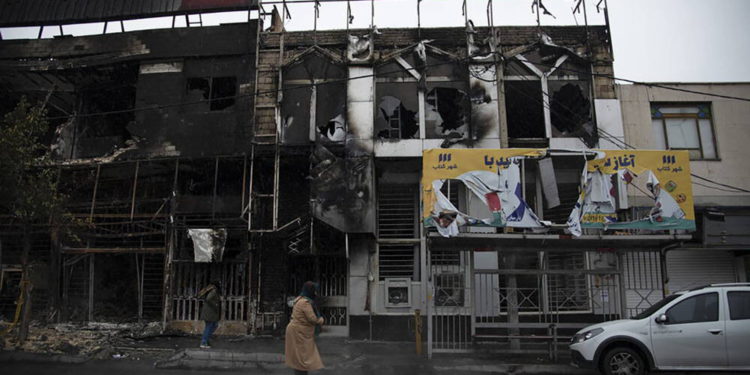 Dos personas caminan el lunes ante edificios quemados durante las protestas, en Teherán. MASOUME ALIAKBAR (AP)