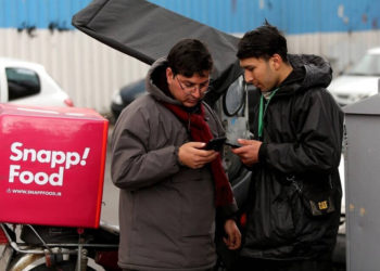 Un mensajero de comida para entregar bicicletas está junto a otro hombre mientras ambos usan teléfonos inteligentes a lo largo de una calle en la capital iraní, Teherán, el 23 de noviembre de 2019. (Atta Kenare / AFP)