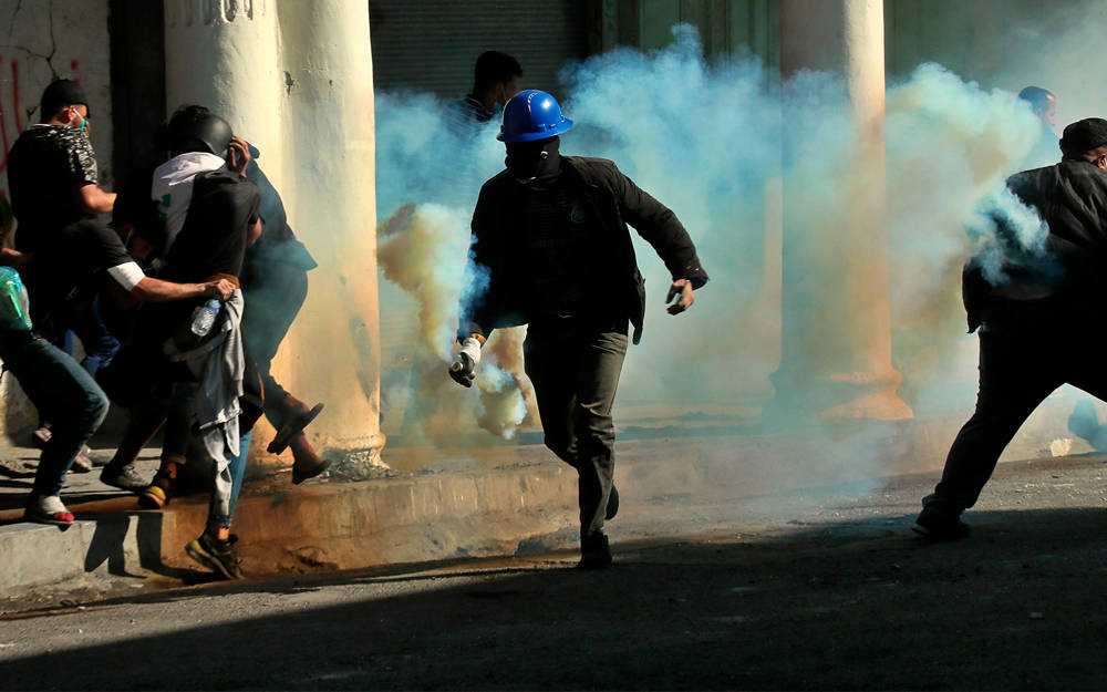 Manifestantes antigubernamentales huyen de gases lacrimógenos disparados por la policía durante enfrentamientos en Bagdad, Iraq, 22 de noviembre de 2019. (AP / Hadi Mizban)
