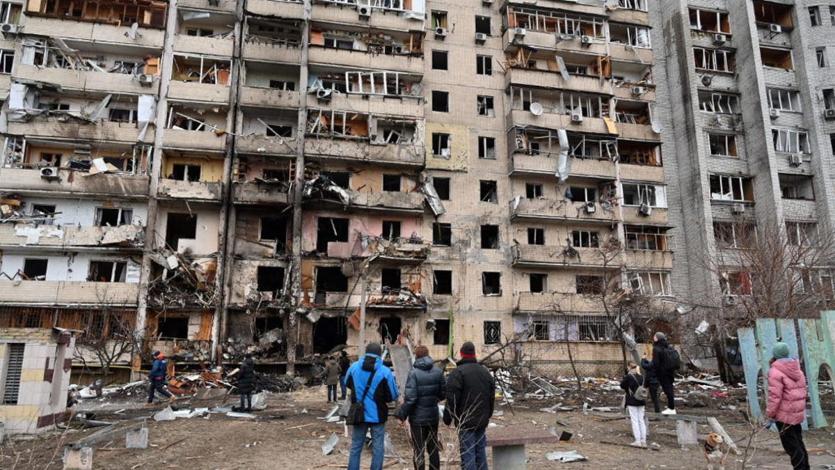Un grupo de personas observa un edificio residencial dañado en la calle Koshytsa, en las afueras de la capital ucraniana, Kiev, donde supuestamente cayó un proyectil militar, el 25 de febrero de 2022. (GENYA SAVILOV / AFP)