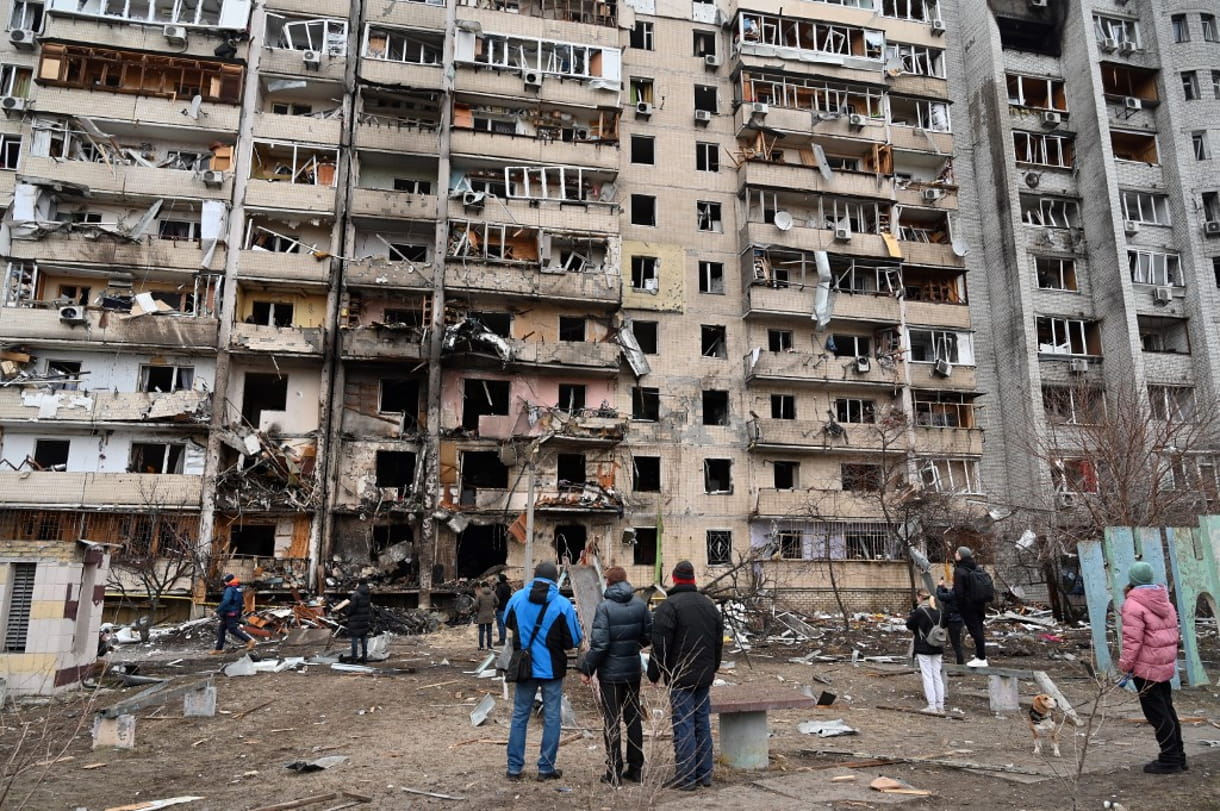 Un grupo de personas observa un edificio residencial dañado en la calle Koshytsa, en las afueras de la capital ucraniana, Kiev, donde supuestamente cayó un proyectil militar, el 25 de febrero de 2022. (GENYA SAVILOV / AFP)