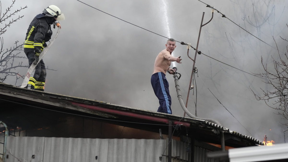 Un hombre ayuda a un bombero a extinguir un granero en llamas tras un bombardeo ruso en las afueras de Mariupol, Ucrania, el jueves 24 de febrero de 2022. (AP Photo/Sergei Grits)