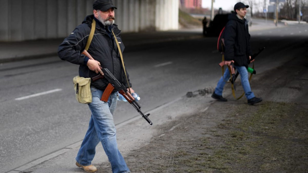 Voluntarios, uno de ellos con un rifle AK-47, protegen una carretera principal que conduce a Kiev el 25 de febrero de 2022 (Daniel LEAL / AFP)
