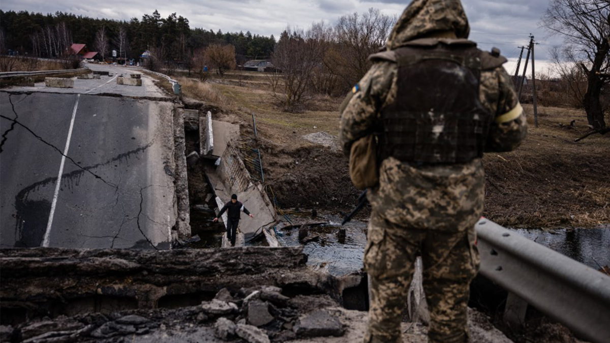 Un soldado ucraniano mira a un civil que cruza un puente volado en un pueblo al este de la ciudad de Brovary, Ucrania, el 6 de marzo de 2022. (Dimitar Dilkoff/AFP)