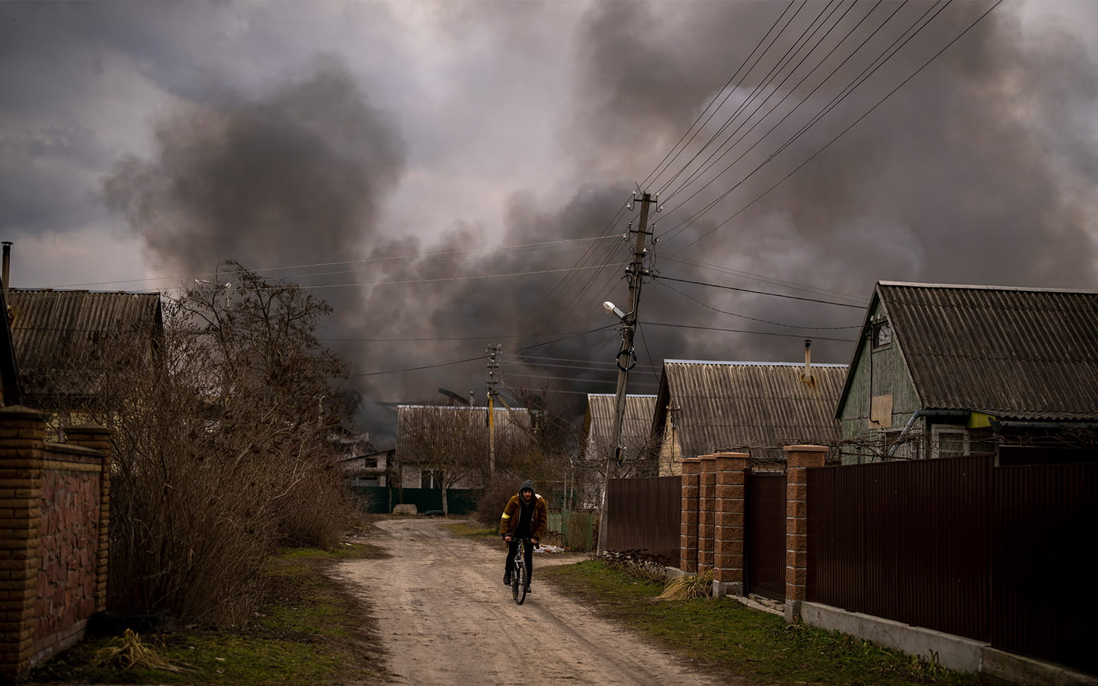 Un hombre ucraniano conduce su bicicleta cerca de una fábrica y una tienda que arden tras ser bombardeadas en Irpin, en las afueras de Kiev, Ucrania, el 6 de marzo de 2022. (AP Photo/Emilio Morenatti)