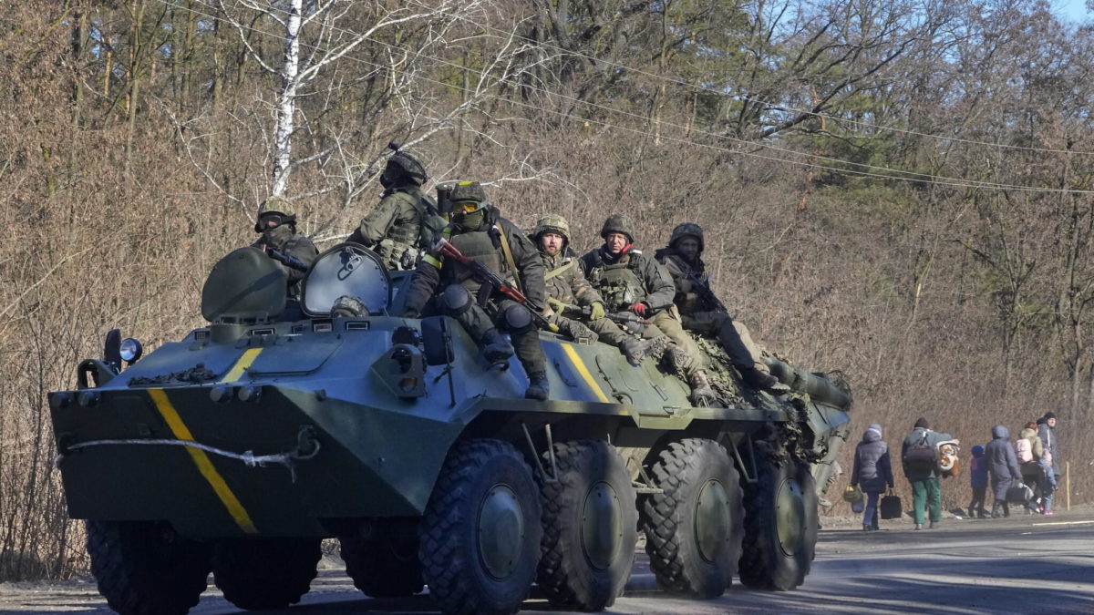 Soldados ucranianos en un vehículo blindado de transporte de personal pasan junto a personas que llevan sus pertenencias mientras huyen del conflicto, en la región de Vyshgorod, cerca de Kiev, Ucrania, el jueves 10 de marzo de 2022. (AP/Efrem Lukatsky)