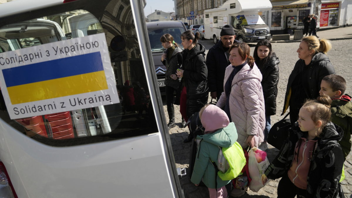 Refugiados ucranianos con niños suben a un transporte en una plaza junto a una estación de tren en Przemysl, Polonia, el 22 de marzo de 2022. (AP Photo/Sergei Grits)