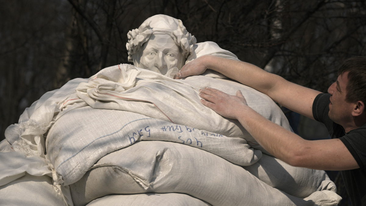 Trabajadores municipales terminan de cubrir una estatua del poeta y filósofo italiano Dante Alighieri con sacos de arena para protegerla de posibles daños por bombardeos, en Kiev, Ucrania, el 23 de marzo de 2022. (AP Photo/Vadim Ghirda)