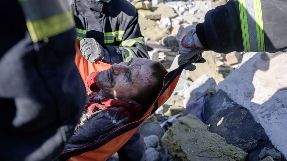 Rescatistas llevan a un soldado ucraniano salvado después de 30 horas de los escombros de la escuela militar alcanzada por cohetes rusos, en Mykolaiv, sur de Ucrania, el 19 de marzo de 2022. (Bulent Kilic/AFP)