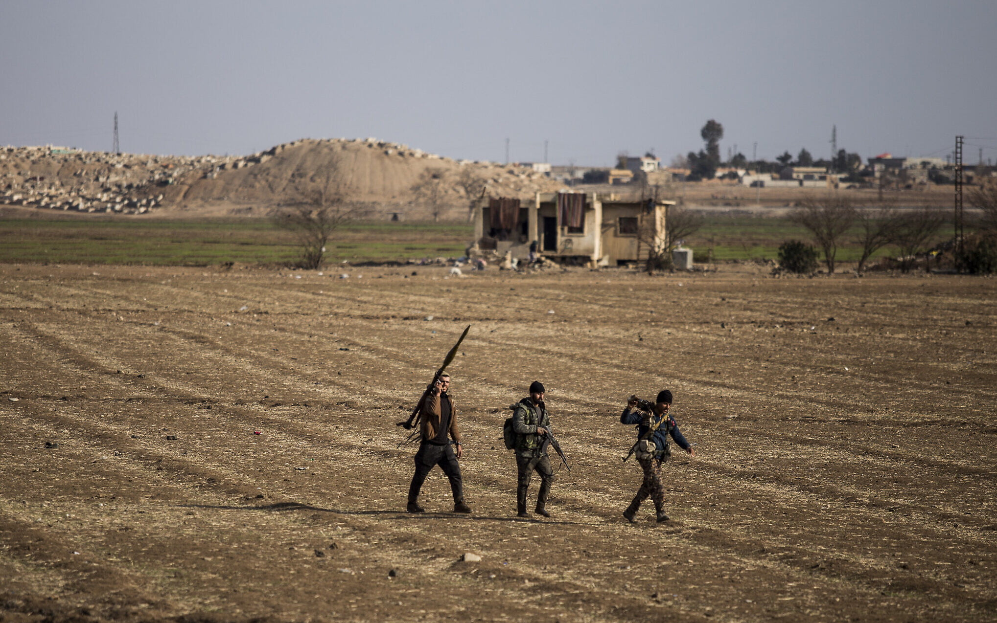 Combatientes de las Fuerzas Democráticas Sirias caminan en un campo en Hassakeh, al noreste de Siria, el 26 de enero de 2022. (AP Photo/Baderkhan Ahmad)