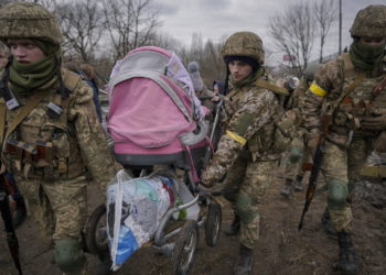 Militares ucranianos llevan un cochecito de bebé después de cruzar el río Irpin por un camino improvisado bajo un puente que fue destruido por un ataque aéreo ruso, mientras ayudan a la gente que huye de la ciudad de Irpin, Ucrania, el 5 de marzo de 2022. (AP Photo/Vadim Ghirda)
