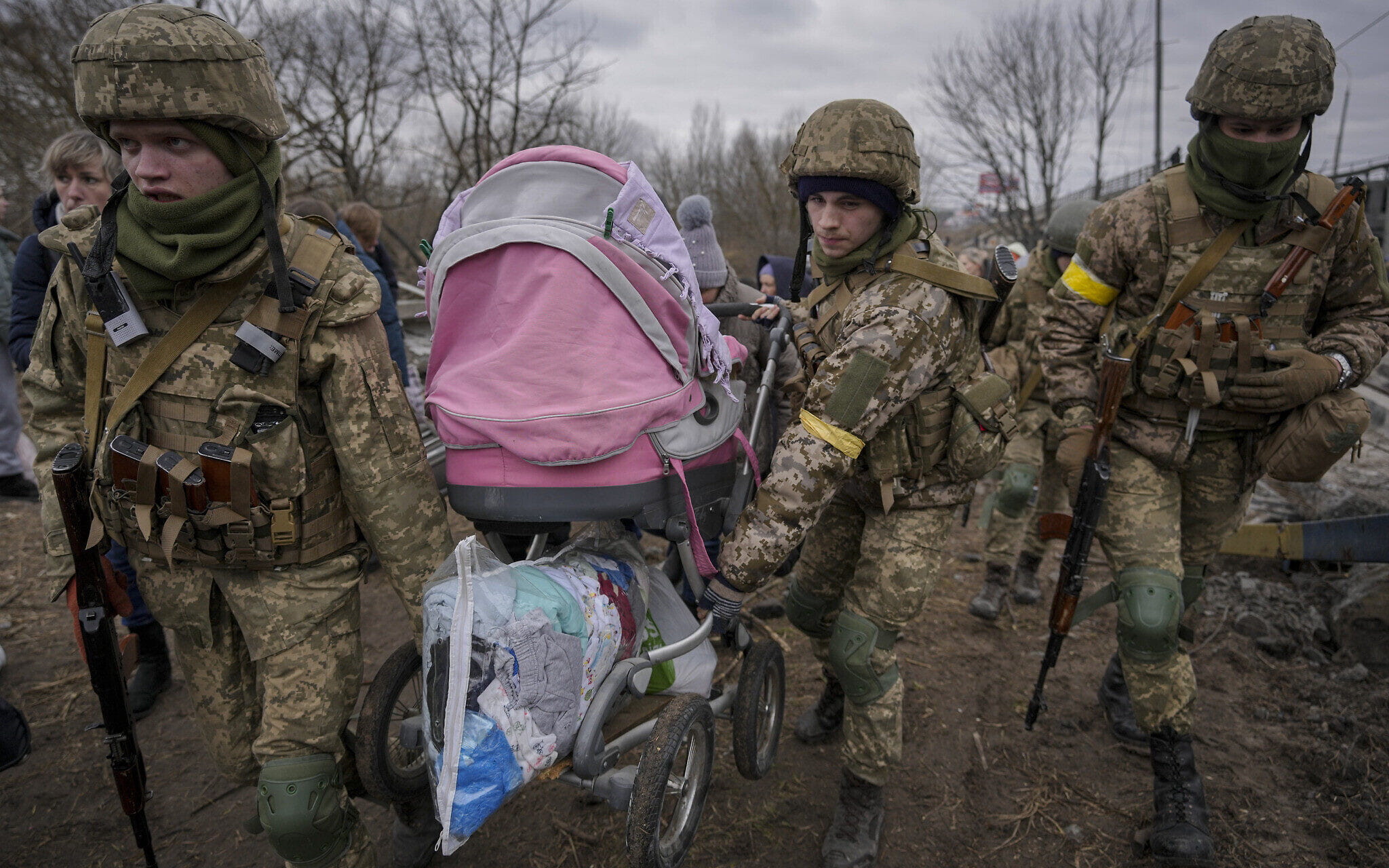 Militares ucranianos llevan un cochecito de bebé después de cruzar el río Irpin por un camino improvisado bajo un puente que fue destruido por un ataque aéreo ruso, mientras ayudan a la gente que huye de la ciudad de Irpin, Ucrania, el 5 de marzo de 2022. (AP Photo/Vadim Ghirda)