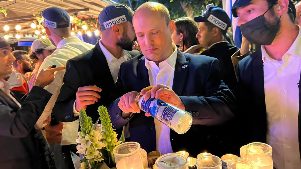 El primer ministro Naftali Bennett enciende una vela conmemorativa mientras asiste a la reapertura del bar Ilka de Tel Aviv días después de que sufriera un ataque terrorista, el 11 de abril de 2022 (Cortesía)