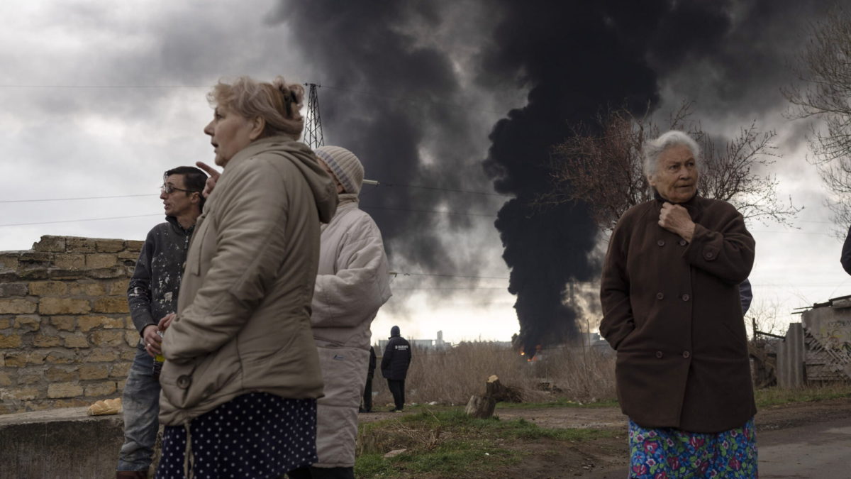 La gente permanece en un patio mientras el humo se eleva en el aire en el fondo después de los bombardeos en Odessa, Ucrania, el domingo 3 de abril de 2022. (AP Photo/Petros Giannakouris)