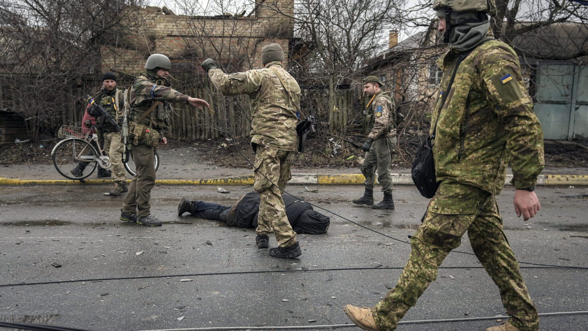 Militares ucranianos sujetan un cable al cuerpo de un civil mientras comprueban si hay trampas explosivas en Bucha, suburbio de Kiev anteriormente ocupado por Rusia, el 2 de abril de 2022. (AP Photo/Vadim Ghirda)