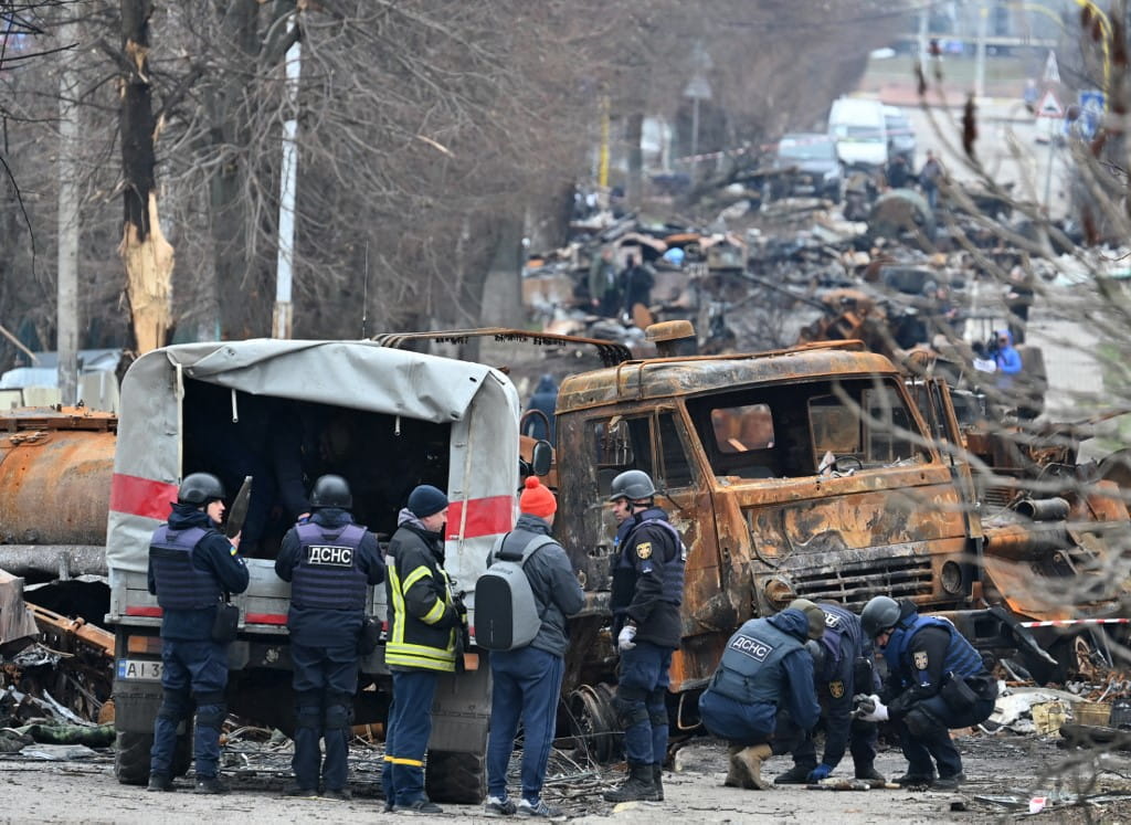 Ingenieros de campo del Servicio Estatal de Emergencias de Ucrania llevan a cabo la limpieza de minas entre los vehículos destruidos en una calle de Bucha el 5 de abril de 2022, mientras las autoridades ucranianas dicen que se han recuperado más de 400 cuerpos de civiles de la región más amplia de Kiev, muchos de los cuales fueron enterrados en fosas comunes (Genya SAVILOV / AFP)