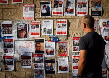 Varias personas caminan cerca de carteles en los que aparecen israelíes retenidos como rehenes por Hamás en Gaza, frente al Ministerio de Defensa en Tel Aviv, 18 de octubre de 2023. (Chaim Goldberg/Flash90)