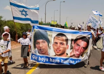Manifestantes marchando con una pancarta que muestra los rostros de la civil israelí cautiva Avera Mengistu, y de los soldados fallecidos Oron Shaul y Hadar Goldin de la ciudad israelí de Ashkelon llegan al kibutz de Karmia el 5 de agosto de 2022. (Jack Guez/AFP)