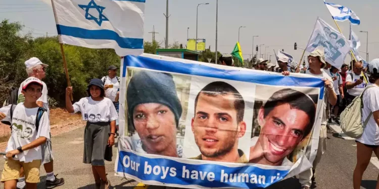 Manifestantes marchando con una pancarta que muestra los rostros de la civil israelí cautiva Avera Mengistu, y de los soldados fallecidos Oron Shaul y Hadar Goldin de la ciudad israelí de Ashkelon llegan al kibutz de Karmia el 5 de agosto de 2022. (Jack Guez/AFP)