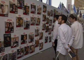 Jóvenes observan fotos de israelíes desaparecidos y retenidos como rehenes en Gaza, expuestas en una pared de Tel Aviv, el viernes 20 de octubre de 2023. (AP Photo/Petros Giannakouris)