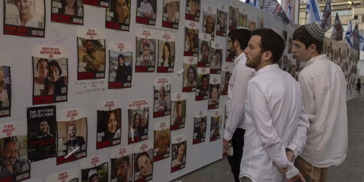 Jóvenes observan fotos de israelíes desaparecidos y retenidos como rehenes en Gaza, expuestas en una pared de Tel Aviv, el viernes 20 de octubre de 2023. (AP Photo/Petros Giannakouris)