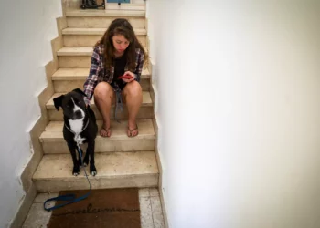 Una mujer y su perro se refugian en una escalera en Jerusalén, mientras suena una sirena de alerta roja durante un bombardeo de cohetes disparados desde Gaza hacia Israel, 7 de octubre de 2023. (Noam Revkin Fenton/Flash90)