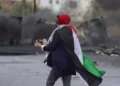 Una mujer envuelta en una bandera palestina se prepara para lanzar piedras hacia las fuerzas israelíes durante los enfrentamientos con ellas en la entrada norte de la ciudad cisjordana de Ramala el 20 de octubre de 2023 (Foto de Jaafar ASHTIYEH / AFP)