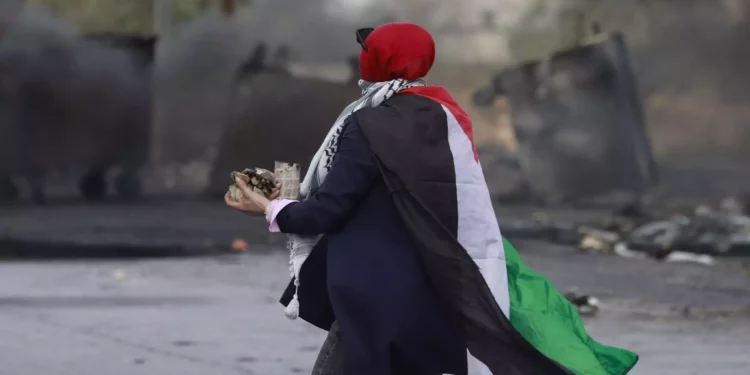 Una mujer envuelta en una bandera palestina se prepara para lanzar piedras hacia las fuerzas israelíes durante los enfrentamientos con ellas en la entrada norte de la ciudad cisjordana de Ramala el 20 de octubre de 2023 (Foto de Jaafar ASHTIYEH / AFP)