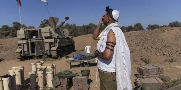 Covered in a prayer shawl, an Israeli soldier prays at an artillery position, near the Israeli-Gaza border, Israel, Monday, Nov. 06, 2023. (AP Photo/Ohad Zwigenberg)