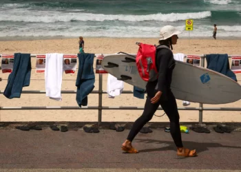 Una surfista con su tabla pasa junto a carteles, toallas y chanclas que forman parte de una protesta organizada por la comunidad judía australiana en la playa de Bondi, en Sídney, el 2 de noviembre de 2023, para poner de relieve la difícil situación de los rehenes retenidos por Hamás (Foto de DAVID GRAY / AFP)